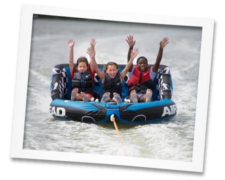 Photo of kids at camp in a raft being pulled by a boat.