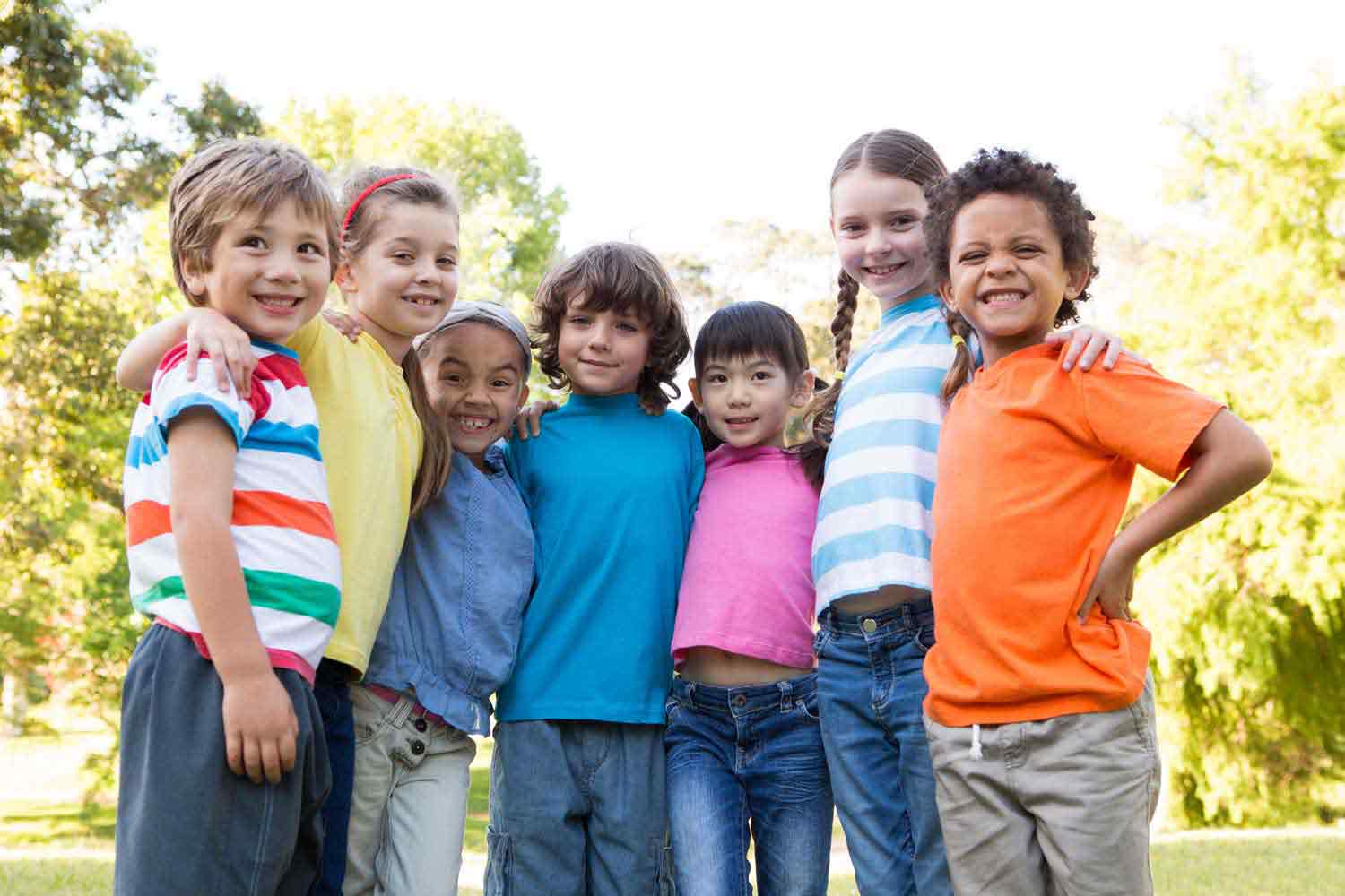 A diverse group of children stand shoulder to shoulder grinning at the camera.