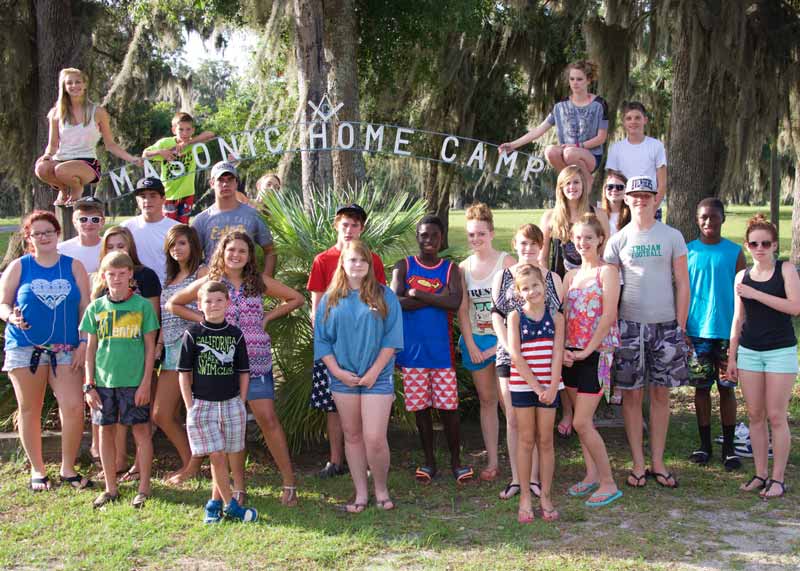 Group of residents stands grouped around the camp entrance signage.